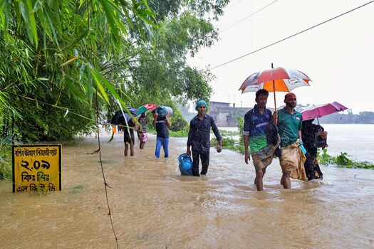 Banshkhali Upazila Chittagong Division Bangladesh 10 July 2026 View of people wading through floodwaters on a rural road carrying umbrellas and belongings during monsoon. Banshkhali Upazila Chittagong Division Bangladesh 10 July 2026 View of people wading through floodwaters on a rural road carrying umbrellas and belongings during monsoon.
