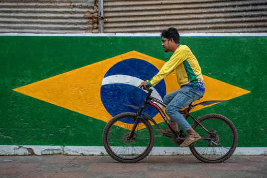 Bogura Bangladesh 02 December 2022 View of a man riding a bicycle past a wall painted with the Brazilian flag in an urban setting.