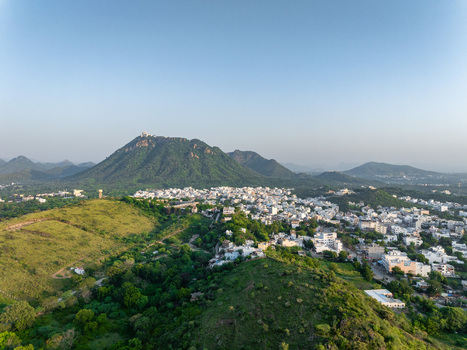 Aerial view of the city of Udaipur nestled among lush green hills and mountains under a clear blue sky in Udaipur Rajasthan India.