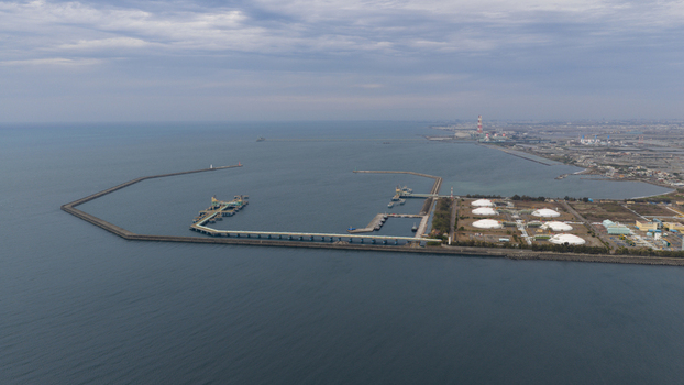 Aerial view of the industrial port and LNG terminal with white storage domes long breakwaters and piers along the coastline in Xingang Village Kaohsiung City Taiwan.