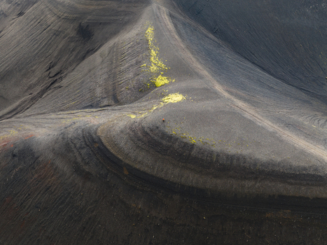 Aerial view of stark undulating terrain with contrasting dark volcanic soil and patches of vibrant green vegetation Highlands Iceland.