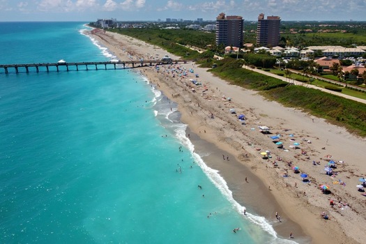 Aerial view of Juno Beach Pier stretching into the turquoise Atlantic Ocean with people on the sandy beach and coastal buildings in Juno Beach Florida United States. Aerial view of Juno Beach Pier stretching into the turquoise Atlantic Ocean with people on the sandy beach and coastal buildings in Juno Beach Florida United States.