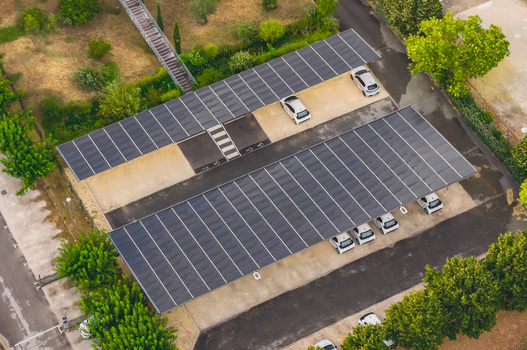 Aerial view of photovoltaic solar panel canopies covering a parking lot with parked cars and surrounding greenery in Alixan Auvergne Rhone Alpes France.