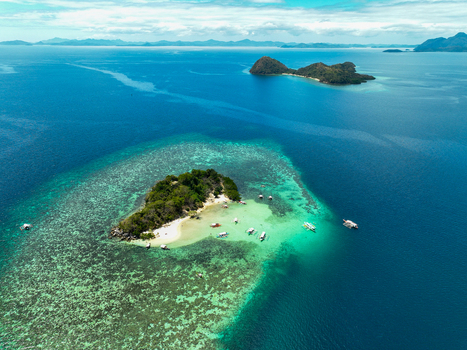 Aerial view of CYC Beach featuring a small island with white sand surrounded by turquoise waters coral reefs and traditional outrigger boats in Coron Mimaropa Philippines. Aerial view of CYC Beach featuring a small island with white sand surrounded by turquoise waters coral reefs and traditional outrigger boats in Coron Mimaropa Philippines.