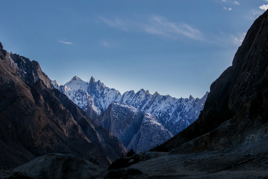 View of the majestic snow capped peaks of the Karakoram range near K2 Base Camp featuring rugged rocky slopes and deep shadows under a clear blue sky in Ghakhar Gilgit Pakistan. View of the majestic snow capped peaks of the Karakoram range near K2 Base Camp featuring rugged rocky slopes and deep shadows under a clear blue sky in Ghakhar Gilgit Pakistan.