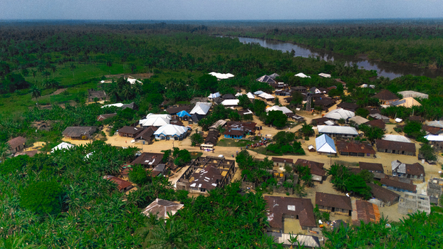 Aerial view of the village of Abua featuring traditional houses with metal roofs surrounded by lush tropical vegetation and a nearby river in Abua Rivers Nigeria. Aerial view of the village of Abua featuring traditional houses with metal roofs surrounded by lush tropical vegetation and a nearby river in Abua Rivers Nigeria.