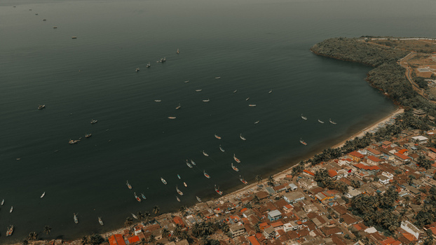 Aerial view of numerous fishing boats anchored in the calm bay along the sandy coastline and dense residential area of Vasco Da Gama Goa India.