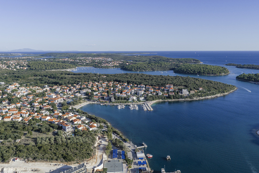 Aerial view of Pjescana Uvala featuring coastal residential houses a marina with boats and lush green forests along the Adriatic Sea in Pula Pjescana Uvala Istarska zupanija Croatia.