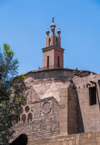 View of the Al Ghuri Dome with its intricate stone carvings and tall minaret under a clear blue sky in Cairo Egypt. View of the Al Ghuri Dome with its intricate stone carvings and tall minaret under a clear blue sky in Cairo Egypt.