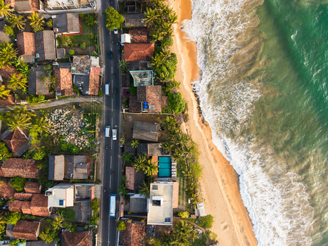 Aerial view of a coastal road lined with houses and palm trees next to a sandy beach and turquoise ocean waves in Galle Southern Province Sri Lanka.