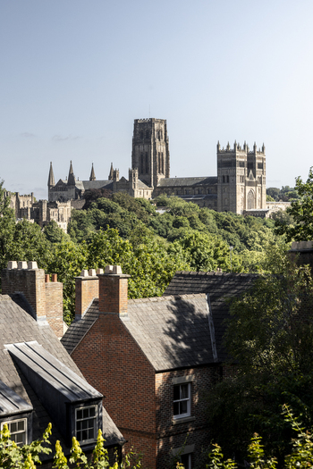 View of Durham Cathedral rising above historic red brick rooftops and lush green trees in Durham England United Kingdom. View of Durham Cathedral rising above historic red brick rooftops and lush green trees in Durham England United Kingdom.