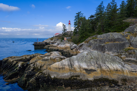 Aerial view of Point Atkinson Lighthouse surrounded by rocky coastline evergreen trees and blue waters of the Pacific Ocean in West Vancouver British Columbia Canada.
