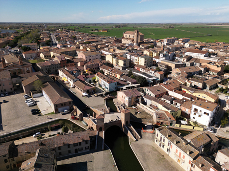 Aerial view of the historic Trepponti bridge and scenic canals surrounded by traditional terracotta rooftops and green fields in Comacchio Emilia Romagna Italy. Aerial view of the historic Trepponti bridge and scenic canals surrounded by traditional terracotta rooftops and green fields in Comacchio Emilia Romagna Italy.