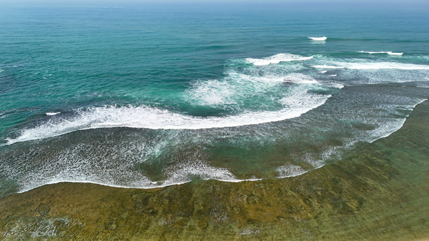 Aerial view of the turquoise waters of a beach with waves breaking over a shallow reef in Indonesia. Aerial view of the turquoise waters of a beach with waves breaking over a shallow reef in Indonesia.
