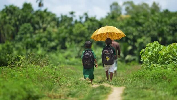 View of school children walking with a yellow umbrella Bangladesh.