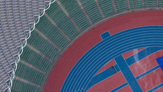 Aerial view of Kaohsiung National Stadium featuring the curved running track with blue and red lanes green spectator seats and solar panel roof Juguang Village Kaohsiung City Taiwan.