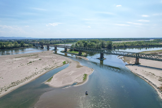 Aerial view of the historic Ponte della Becca iron truss bridge crossing the river Po with exposed sandbanks and green trees in Linarolo Lombardia Italy.