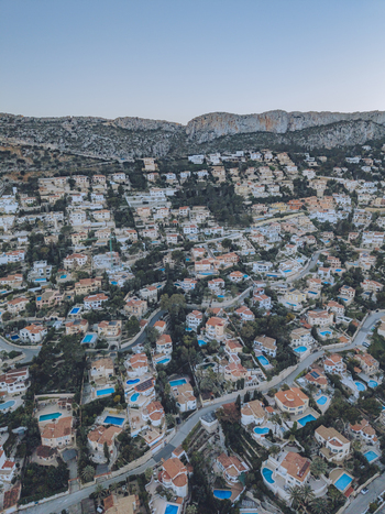 Aerial view of a hillside residential neighborhood featuring numerous villas with private swimming pools winding roads and rocky terrain in Calp Valencian Community Spain. Aerial view of a hillside residential neighborhood featuring numerous villas with private swimming pools winding roads and rocky terrain in Calp Valencian Community Spain.