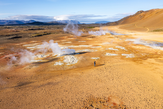 Aerial view of Hverir geothermal field with steaming fumaroles bubbling mud pots and a lone person walking across the orange volcanic landscape Reykjahlid Thingeyjarsveit Iceland.