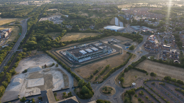 Aerial view of a modern data center facility surrounded by green fields suburban housing and road networks in Bracknell England United Kingdom.