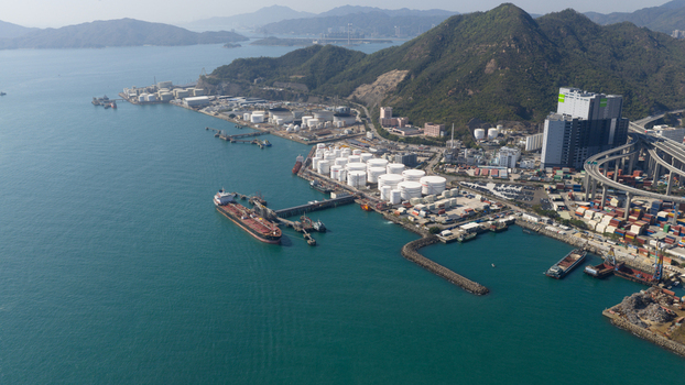 Aerial view of industrial oil storage tanks and a large tanker ship docked at the terminal near green mountains and a highway viaduct Hong Kong Hong Kong. Aerial view of industrial oil storage tanks and a large tanker ship docked at the terminal near green mountains and a highway viaduct Hong Kong Hong Kong.