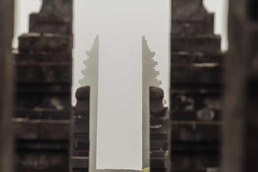 View of the symmetrical stone split gateway of Cetho Temple against a misty white background in Kecamatan Jenawi Jawa Tengah Indonesia. View of the symmetrical stone split gateway of Cetho Temple against a misty white background in Kecamatan Jenawi Jawa Tengah Indonesia.