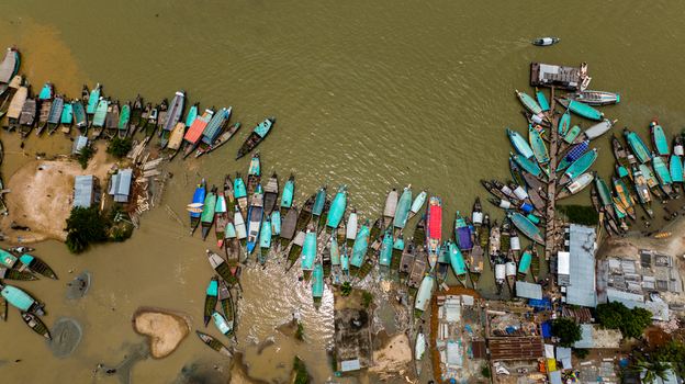 Aerial view of Baish Mowza Sarak Bazar with numerous wooden boats docked along the riverbank in Nabinagar Chittagong Division Bangladesh. Aerial view of Baish Mowza Sarak Bazar with numerous wooden boats docked along the riverbank in Nabinagar Chittagong Division Bangladesh.