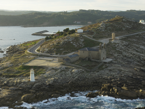 Aerial view of a historic stone monastery and a lighthouse situated on a rocky coastline in Galicia Spain.