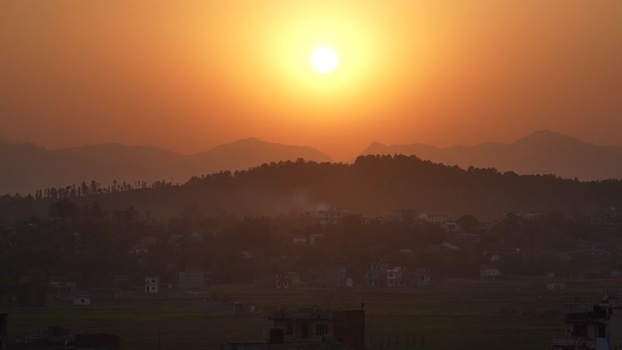 View of sunset over silhouetted hills and a village Nepal.