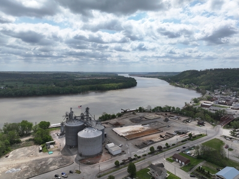 Aerial view of industrial grain silos on the riverbank with the winding river and lush green hills under a cloudy sky in Aurora Indiana United States. Aerial view of industrial grain silos on the riverbank with the winding river and lush green hills under a cloudy sky in Aurora Indiana United States.