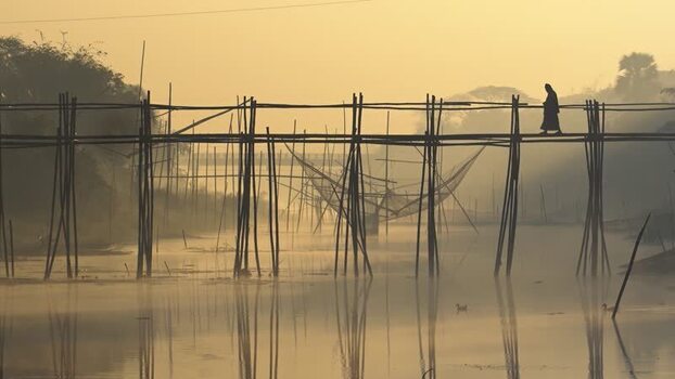 View of a person walking on a bamboo bridge at sunrise Bangladesh.