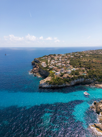 Aerial view of the coastal houses and rocky cliffs overlooking the turquoise waters of the Mediterranean Sea Cala Llombards Illes Balears Spain. Aerial view of the coastal houses and rocky cliffs overlooking the turquoise waters of the Mediterranean Sea Cala Llombards Illes Balears Spain.