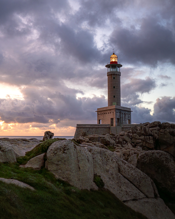 View of the Faro de Punta Nariga lighthouse standing on a rocky coastline under a dramatic sunset sky with glowing lantern light Malpica A Coruna Spain. View of the Faro de Punta Nariga lighthouse standing on a rocky coastline under a dramatic sunset sky with glowing lantern light Malpica A Coruna Spain.