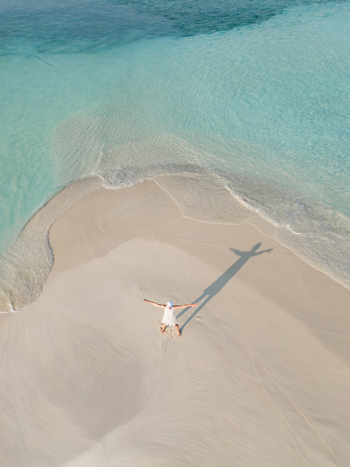 Aerial view of a solitary figure sprawled on the white sand beach meeting the turquoise sea in a vibrant display of color Dhidhdhoo Thiladhunmathi Atoll Maldives.