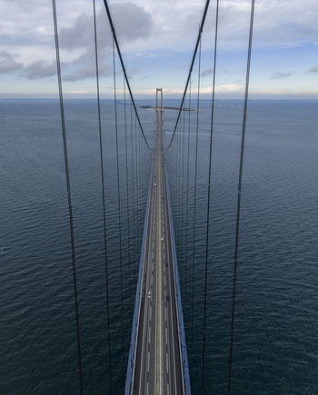Aerial view of the Great Belt Bridge with its massive suspension cables and cars driving across the dark blue sea under a cloudy sky Denmark. Aerial view of the Great Belt Bridge with its massive suspension cables and cars driving across the dark blue sea under a cloudy sky Denmark.