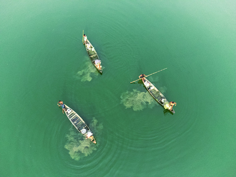Khansama Upazila Bangladesh 12 September 2023 Aerial view of three traditional wooden boats with fishermen on the calm green waters of a river.