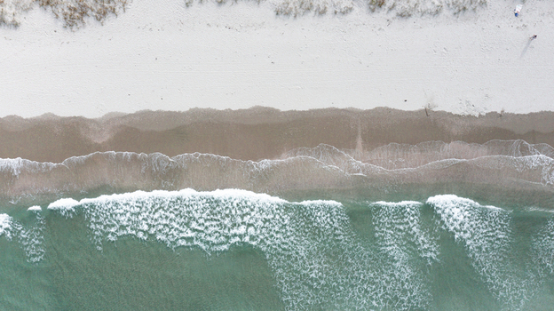 Aerial view of the sandy shoreline and turquoise waves crashing on Omaha Beach Omaha Auckland New Zealand.