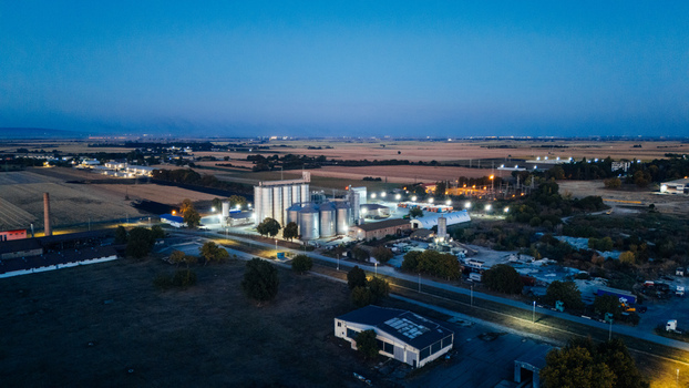 Aerial view of an industrial facility with illuminated grain silos surrounded by agricultural fields at dusk in Sremska Mitrovica Vojvodina Serbia. Aerial view of an industrial facility with illuminated grain silos surrounded by agricultural fields at dusk in Sremska Mitrovica Vojvodina Serbia.