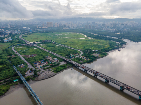 Aerial view of the bridge crossing the creek in Thane with heavy traffic lush green wetlands and the urban skyline in the background in Thane Maharashtra India. Aerial view of the bridge crossing the creek in Thane with heavy traffic lush green wetlands and the urban skyline in the background in Thane Maharashtra India.