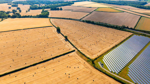 Aerial view of golden wheat fields dotted with hay bales and a large solar farm under a clear sky in Dorset England United Kingdom. Aerial view of golden wheat fields dotted with hay bales and a large solar farm under a clear sky in Dorset England United Kingdom.