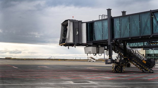 View of a modern jet bridge standing on an airport tarmac under a cloudy sky in Iceland.