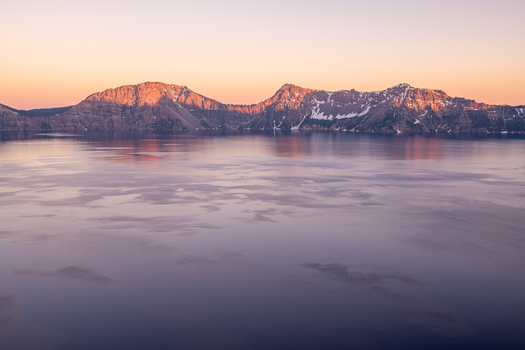 View of tranquil waters reflecting the soft pastel hues of dawn kissing the rugged peaks painting the horizon with warmth and serenity Crater Lake Oregon United States. View of tranquil waters reflecting the soft pastel hues of dawn kissing the rugged peaks painting the horizon with warmth and serenity Crater Lake Oregon United States.