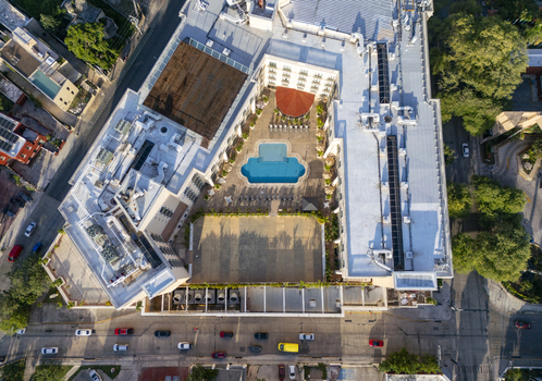 Aerial view of a hotel building with a central courtyard featuring a swimming pool surrounded by city streets and lush trees in Merida Yucatan Mexico. Aerial view of a hotel building with a central courtyard featuring a swimming pool surrounded by city streets and lush trees in Merida Yucatan Mexico.