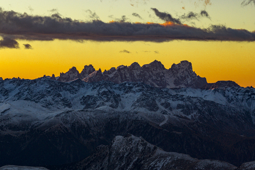 Aerial view of jagged peaks pierce the golden horizon dusted with snow creating a stark contrast against the deep shadows below South Tyrol Dolomites Trentino Alto Adige Italy.