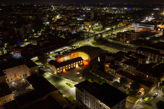 Aerial view of the Enzo Ferrari Museum illuminated at night featuring its iconic yellow curved roof and surrounding historic buildings in Modena Emilia Romagna Italy. Aerial view of the Enzo Ferrari Museum illuminated at night featuring its iconic yellow curved roof and surrounding historic buildings in Modena Emilia Romagna Italy.