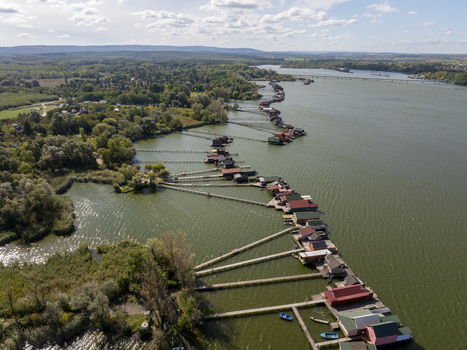 Aerial view of the colorful wooden houses on stilts at Bokodi Floating Village connected by long wooden piers over the calm lake water in Oroszlany Hungary. Aerial view of the colorful wooden houses on stilts at Bokodi Floating Village connected by long wooden piers over the calm lake water in Oroszlany Hungary.