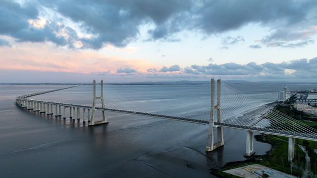 Aerial view of the Vasco da Gama Bridge spanning the Tagus River under a dramatic cloudy sky at sunset in Lisboa Portugal.