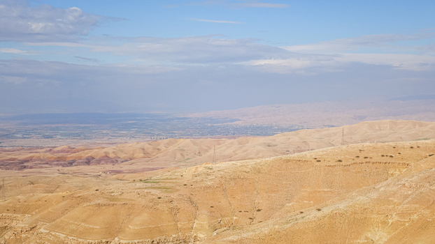 View of the arid desert landscape and rolling hills near Wadi Musa featuring rugged terrain sparse vegetation and distant hazy mountains in Wadi Musa Ma an Governorate Jordan. View of the arid desert landscape and rolling hills near Wadi Musa featuring rugged terrain sparse vegetation and distant hazy mountains in Wadi Musa Ma an Governorate Jordan.