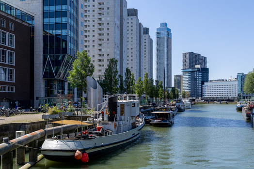 View of a vintage boat moored in a canal surrounded by modern skyscrapers and residential buildings under a clear blue sky Rotterdam South Holland Netherlands. View of a vintage boat moored in a canal surrounded by modern skyscrapers and residential buildings under a clear blue sky Rotterdam South Holland Netherlands.