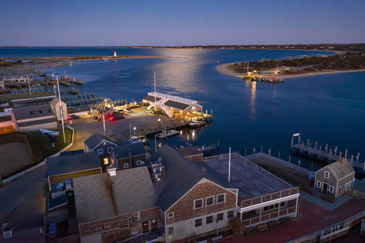 View of Martha s Vineyard harbor and Edgartown waterfront with historic buildings docks and a distant lighthouse at dusk in Edgartown Massachusetts United States.
